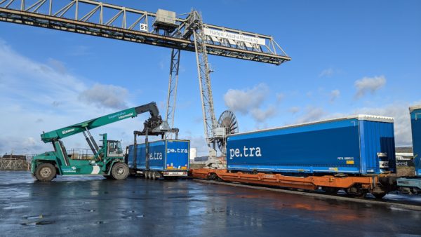 A reach stacker unloads a blue semi-trailer from a train and places it on a truck at bayernhafen Aschaffenburg