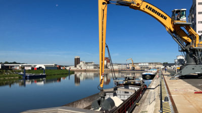 Mobilbagger taucht Greifer in Binnenschiff
