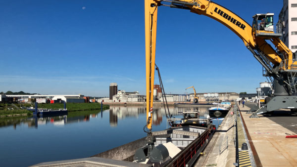 Mobilbagger taucht Greifer in Binnenschiff