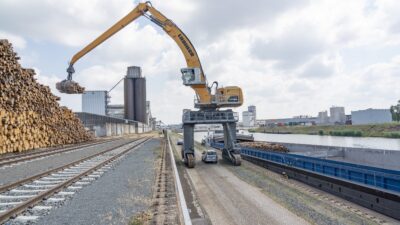 Mobilbagger verlädt Holzstämme auf ein Binnenshciff